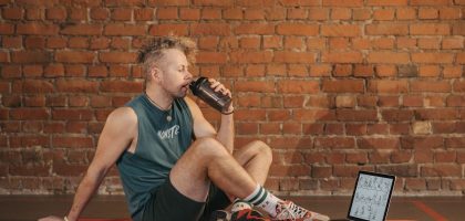 Athletic man sitting on exercise mat with water bottle, taking a break from workout, in a rustic indoor setting.