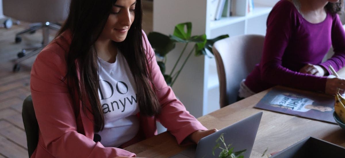 Two women working at laptops in a stylish office space, focused and productive.